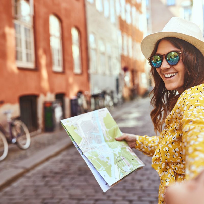 POV of a young woman holding a map and smiling while leading a person by the hand through city streets
